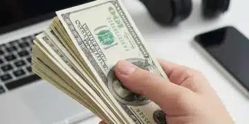 Hand holding money with electronics in background, representing manufacturer rebate savings.